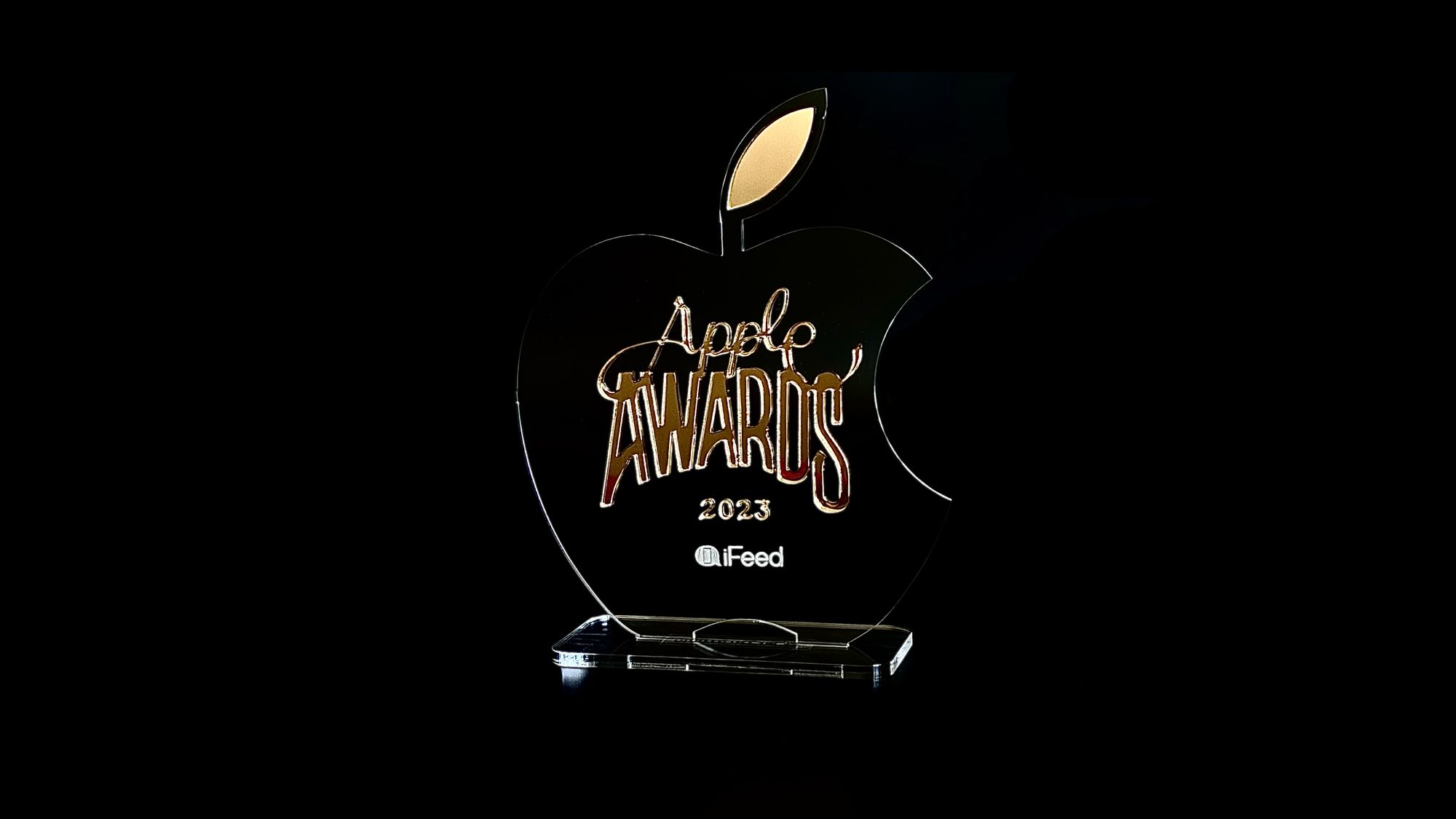 Logo dos iFeed Apple Awards 2023, no centro de uma versão transparente do logo da Apple, sobre um iPhone deitado.