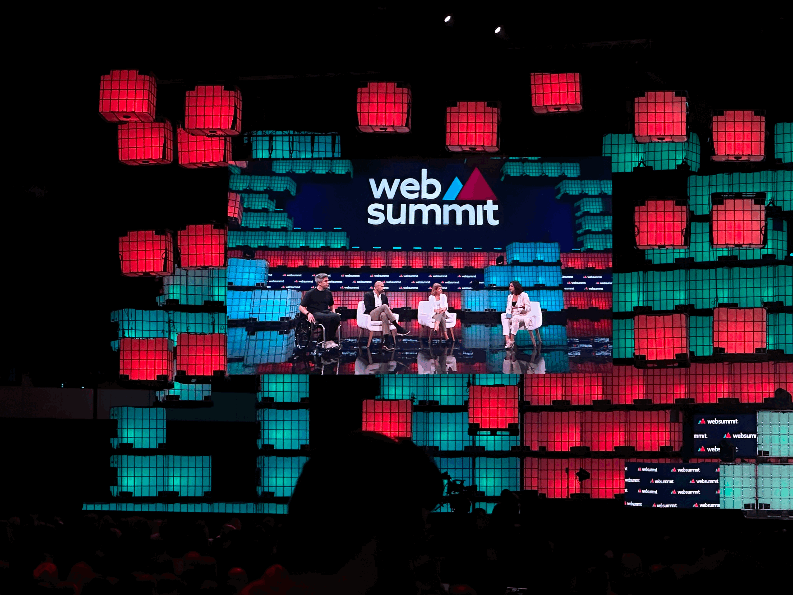 Ecrã do palco principal da Web Summit 2023. Veem-Hiroki Takeuchi, Samir El-Sabini, Iana Dimitrov e Anne Gaviola no palco.