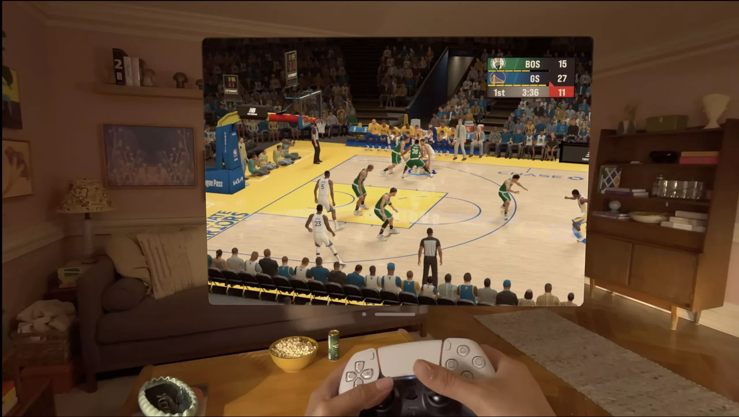 Mãos a segurar um comando da PS5 numa sala. À frente, um ecrã suspenso com um jogo de basquetebol do NBA2K.
